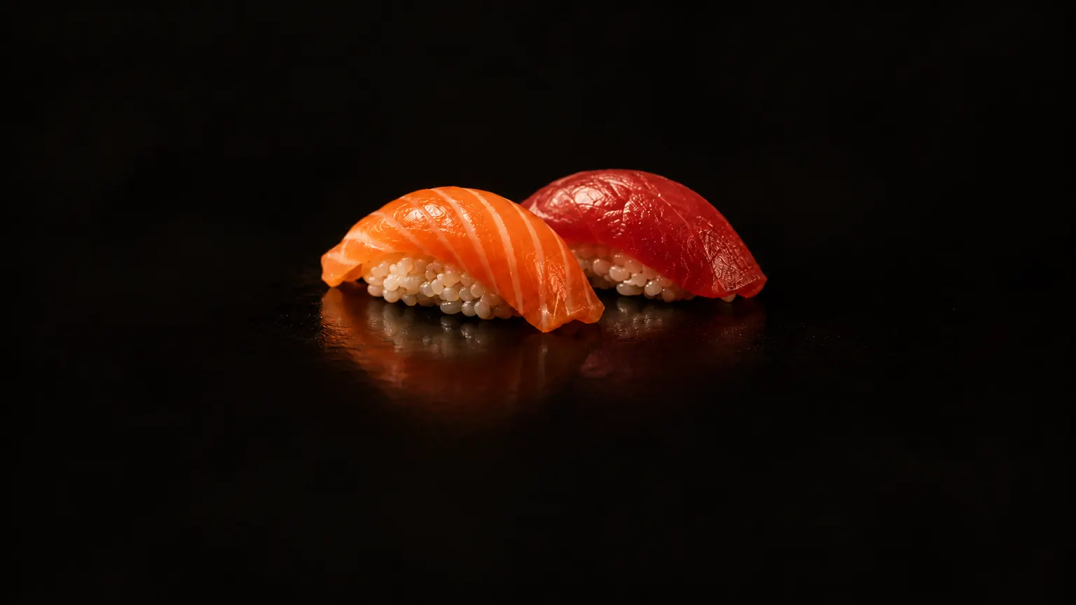 Two pieces of nigiri, salmon and tuna, on black lacquer in a single beam of light.